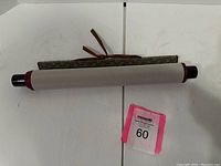 The scroll rolled up with decorative fabric and wooden ends visible alongside a pink lot number tag.