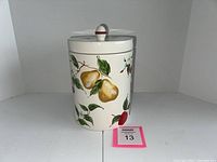 Side view of the cylindrical StoneLite kitchen canister showing hand-painted pears, apples, and green leaves on a white background.