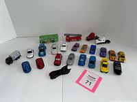 Photo showing entire lot of 21 toy vehicles arranged on a white background, including cars, trucks, buses, and specialty vehicles such as Batman car and police training truck.