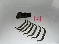 Old black metal woodworking plane with curved handle, placed behind seven ornate metal handles arranged in a row.