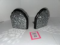 Pair of mirror tiled bookends with black frames placed on a white surface showing their mosaic reflective tile patterns and the curved top design. One bookend positioned slightly behind the other.