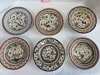 Top view showing all six plates arranged in two rows; clear view of hand-painted animal and floral designs with vibrant border colors.