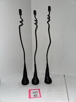 Front view of three tall forged iron candlesticks with twisting abstract vine-like shafts and round bases, set against a white backdrop.