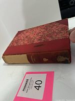 Side view of a red-bound book with marbled cover and worn spine, visible damage to cloth binding.