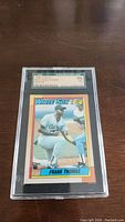 Front view of 1989 Topps Frank Thomas Rookie baseball card graded SGC 84 in protective plastic case on wooden surface.