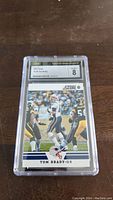 Front side of the 2012 Tom Brady Score football card showing the image of Tom Brady during a game, protected in a clear plastic CSG graded slab with rating 8.