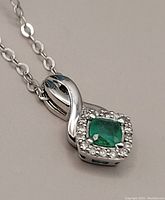 Close-up view of the 10K white gold pendant with square emerald and diamond halo on the chain against neutral background