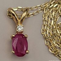 Close-up of pendant showing oval red ruby and small round diamond accent on yellow gold setting
