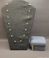 Full view of necklace displayed on grey bust with velvet storage box beside it.