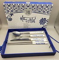 Cutlery set displayed in open decorative box showing fork, spoon, knife, and chopsticks with blue and white floral handles