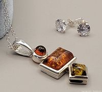 Close-up of amber pendant and cubic zirconia stud earrings on a gray surface showing stone colors and silver settings