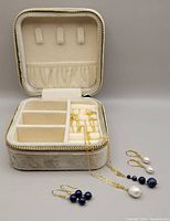 Open jewelry storage box with multiple compartments. Two pairs of earrings and two chains with pendants placed in front.
