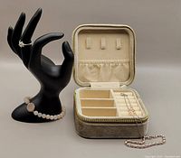 Black hand display holding ring and stretch bracelet beside a zippered velvet storage box with compartments