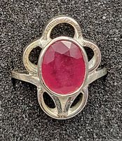 Close-up of sterling silver ring featuring large oval faceted ruby gemstone in ornate silver setting.