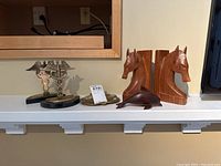 Display of all lot items including wooden horse bookends, caduceus bookends, wooden dolphin, and brass inkwell on white shelf.