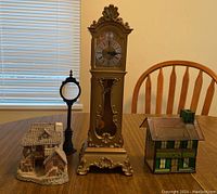 Miniature clock, ceramic cottage, leaded glass house, and black pen with magnifier on wooden table.