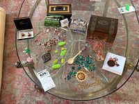Photo showing costume jewelry items arranged on a glass table including bead necklaces, cuff links, miniature purses, and jewelry boxes.