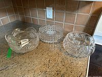 Three clear glass decorative bowls on kitchen countertop showing different cut glass patterns and scalloped edges.