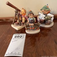 Three Goebel figurines placed on a wooden surface, showing their relative sizes and details.