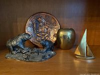 Photo showing the bear sculpture, ceramic plate with Aztec/Mayan design, brass vase, and brass sailboat figurine arranged on a wooden shelf.
