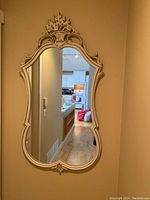 Full view of the ornate framed wall mirror installed on a beige wall, showing its height and decorative frame.