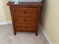 Front view of wooden nightstand showing three drawers with black knobs.