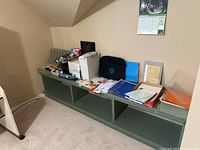 Wide-angle of green shelves holding various folders, paper, organizers, stamps, and stationery items against a beige wall.