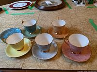 Five Royal Albert Gossamer bone china teacups on their matching saucers in pastel colors arranged on table.