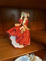 Front angle of Royal Doulton Top O' the Hill figurine showing woman in red dress holding hat.