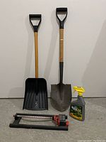 Full lot showing two shovels, oscillating sprinkler, and Weed Out spray bottle on floor against white wall.