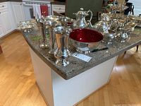 Multiple silverplate trumpet vases, bowl, and salt and pepper shakers arranged on countertop