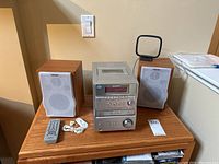 Front view of Sony compact stereo system including CD player, cassette player, two speakers, remote, antenna, and cables placed on wooden surface.