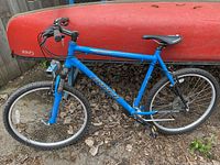 Blue Norco bicycle against a fence with red canoe, showing side profile including frame, tires, seat, and handlebars.