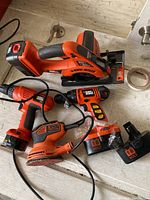 Black & Decker cordless tools including trim saw, two drills, corded detail sander, and batteries on table surface
