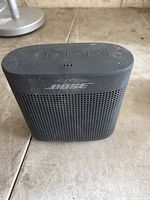 Front view of compact black Bose Bluetooth speaker showing Bose logo and top control buttons with dust and surface wear.
