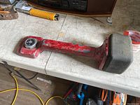 Red carpet installation knee kicker placed on a white table with visible wear and with a compass attached.