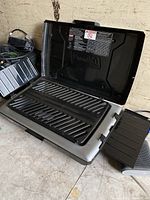 Open Coleman camp grill stove showing cooking grate and fold-out side shelves