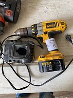 Yellow and black DeWalt 14.4V hammer drill with attached battery and corresponding black battery charger with power cord