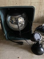 Disco ball inside the green plastic case with power cord and light projector cords coiled inside the case.