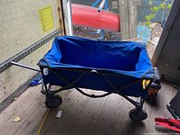 Foldable blue utility wagon fully extended, showing metal frame and fabric body on four wheels.