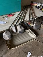 Seven golf drivers laid out on the floor showing shafts and club heads, various brands visible.