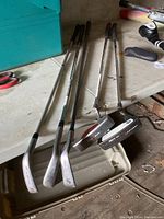 Overview of the set of 5 golf clubs on a surface including irons and putters, showing shafts and club heads.