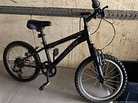 Side view of the black and purple kids CCM mountain bike showing front suspension fork, 6-speed gear system, padded seat and knobby tires.
