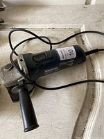 Photo of a Mastercraft branded electric angle grinder with power cord and side handle, resting on a wooden surface.