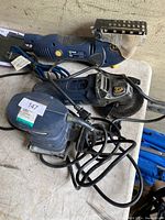 Photo showing a blue Mastercraft angle grinder (missing handle) needing repair, a blue Mastercraft orbital sander, and a Mastercraft precision saw with sanding attachment, all on a workbench.