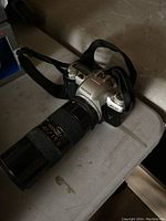 Pentax MZ-50 35mm film camera with long zoom lens attached, resting on table surface.