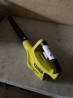 Yellow Ryobi battery-powered leaf blower without batteries on a gray table.
