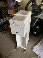 White SodaStream carbonation machine with button control and textured front panel shown on floor with other items in background.