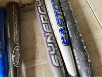 Photo showing three softball bats side by side on a beige floor, detailed brand logos of Easton, Louisville Slugger, and Rawlings visible.