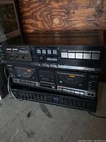 Photo of a stacked vintage Sony audio system including a cassette deck with dual tape compartments, a receiver, and an equalizer unit, all black with labeled buttons and sliders.